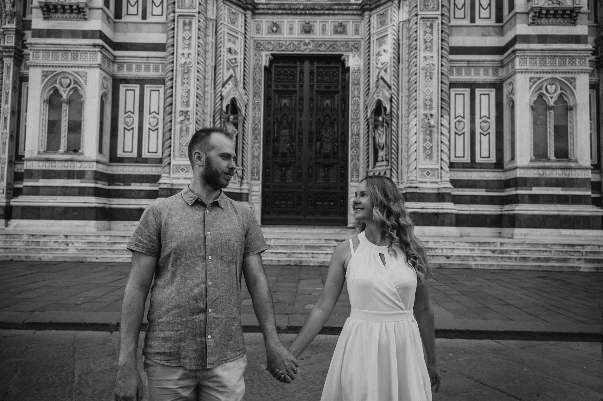 Black-and-white photograph of the couple walking hand in hand in front of the Duomo during their Florence couple photoshoot.