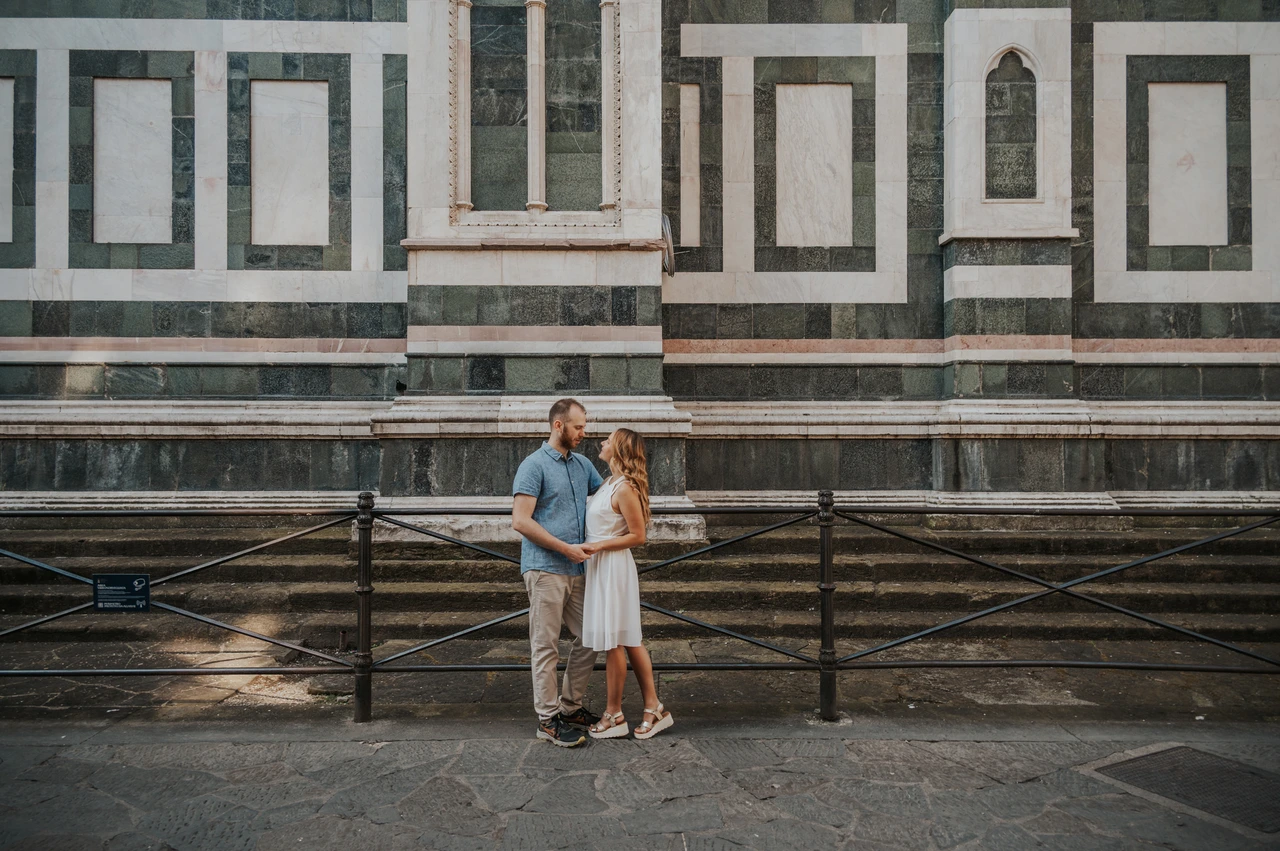 Florence couple photoshoot with an embrace beside patterned marble A wide view shows the couple embracing beside the cathedral’s patterned marble wall during their Florence photoshoot.