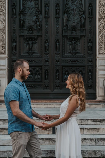 Florence couple photoshoot holding hands by the carved doorway The couple face each other and hold both hands beside the cathedral’s carved door during their Florence photoshoot.