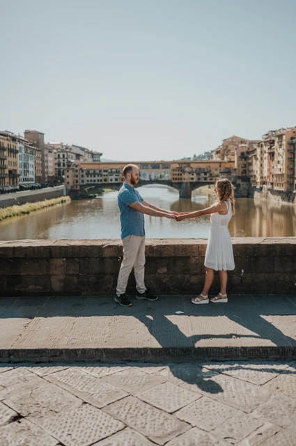 Holding hands by the Arno during a Florence couple photoshoot The couple face each other and hold hands by the river parapet, with Ponte Vecchio behind them, during their Florence photoshoot.