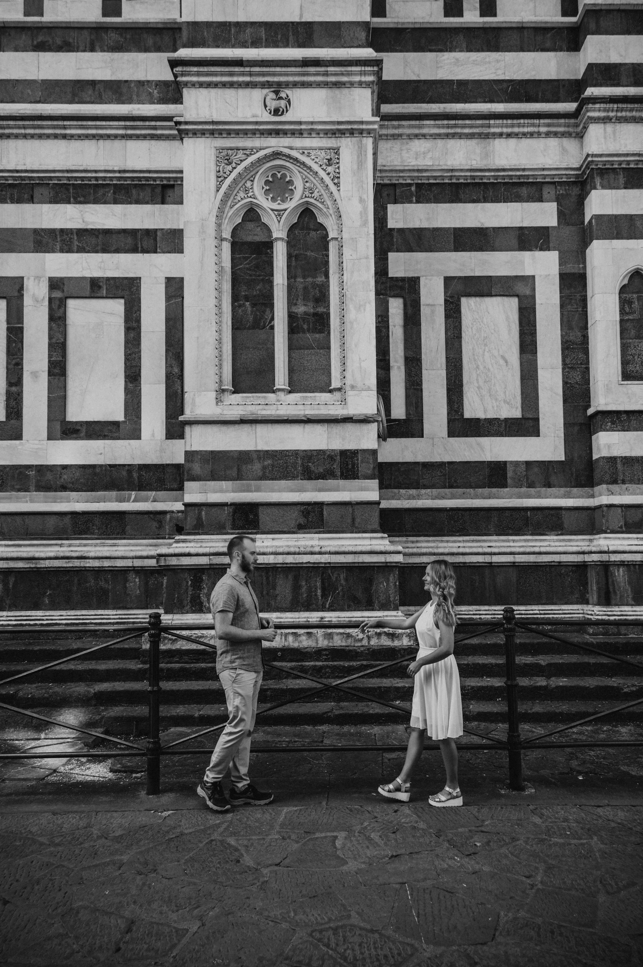 Black-and-white photograph of the couple beside a railing and striped marble wall during their Florence photoshoot.