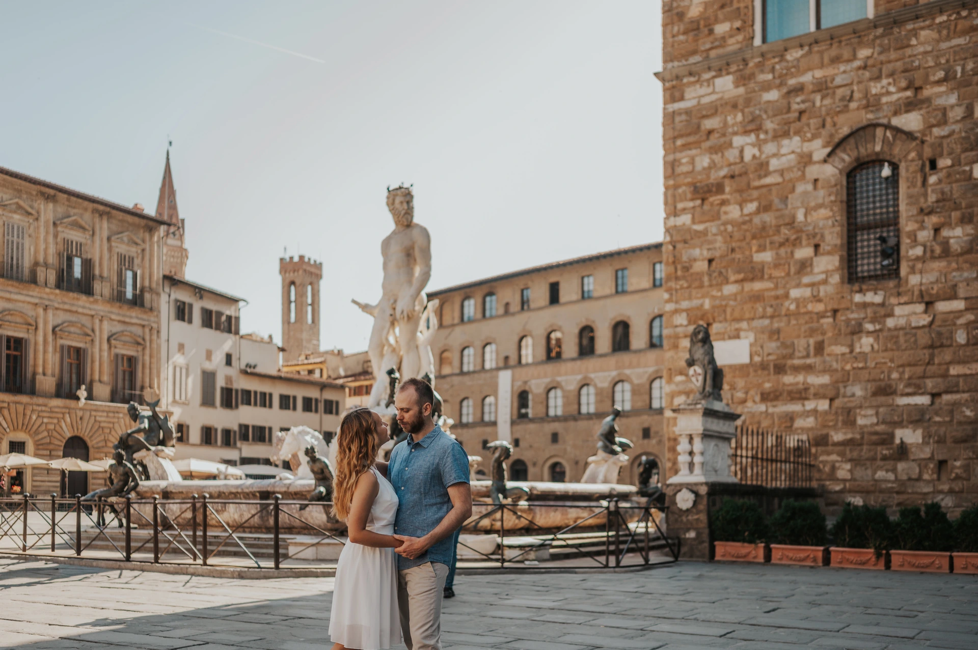 The couple stand together near the Neptune Fountain with Palazzo Vecchio to one side during their Florence couple photoshoot.