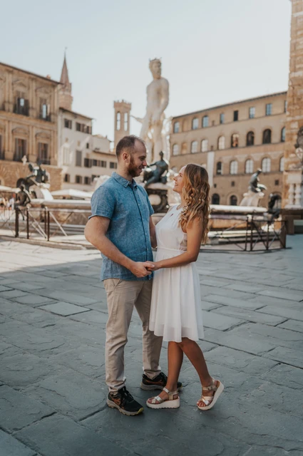 A playful piazza portrait during a Florence couple photoshoot The couple hold hands and lean towards each other in Piazza della Signoria during their Florence photoshoot.