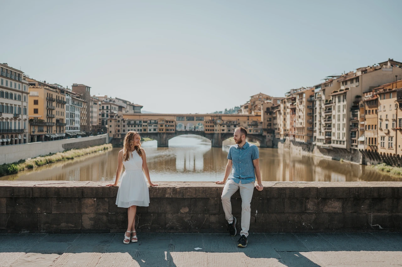 Florence couple photoshoot overlooking the Arno and Ponte Vecchio The couple stand by the stone parapet above the Arno, with Ponte Vecchio in the background, during their Florence couple photoshoot.