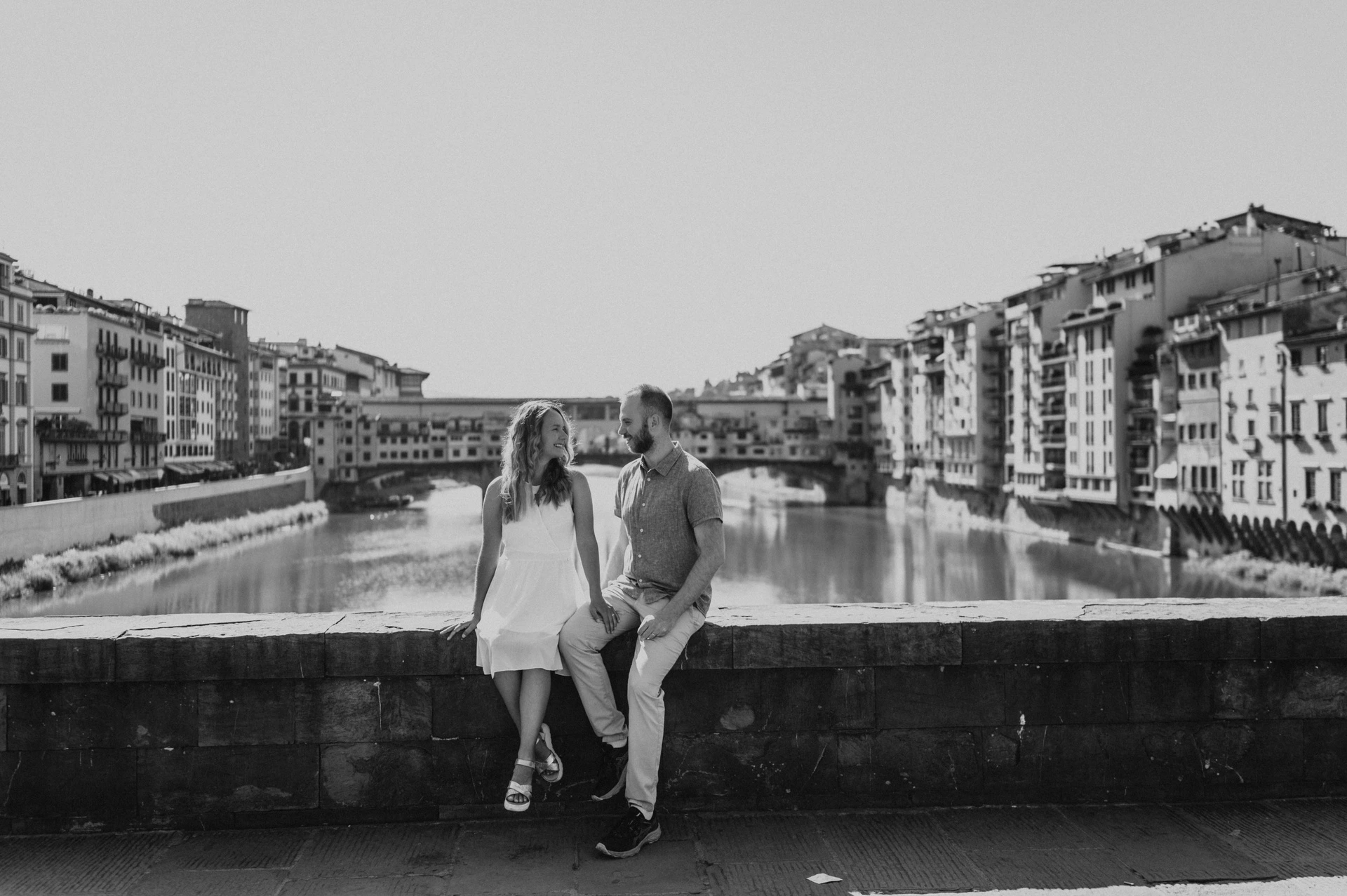 Black-and-white photograph of the couple together at the river parapet with Ponte Vecchio behind them during their Florence photoshoot.