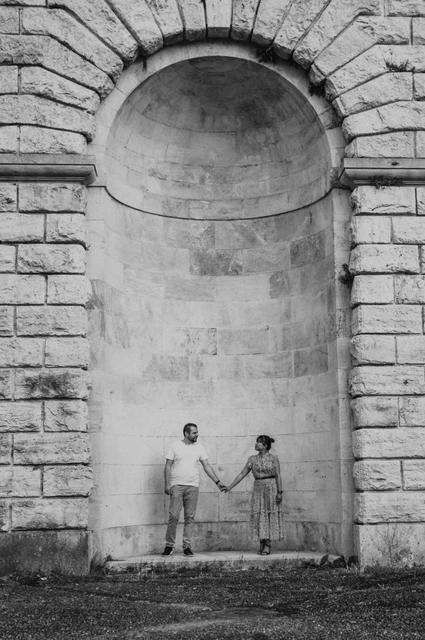 Black-and-white Florence photoshoot of the couple holding hands beneath a tall arched recess, surrounded by textured stone blocks.