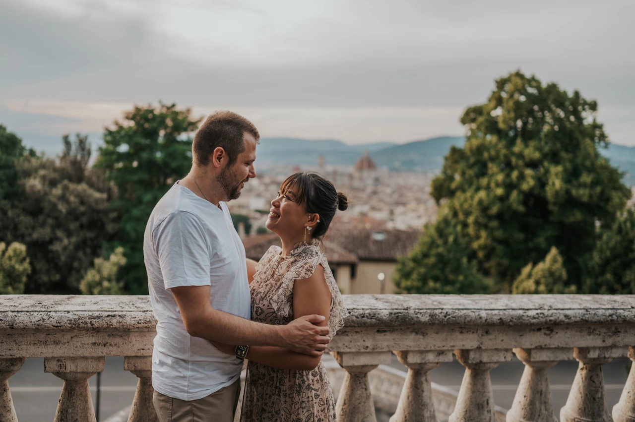 Florence photoshoot portrait framed by trees and stone The couple face one another in an embrace during their Florence photoshoot, with the balustrade, leafy trees and rooftops across the background.