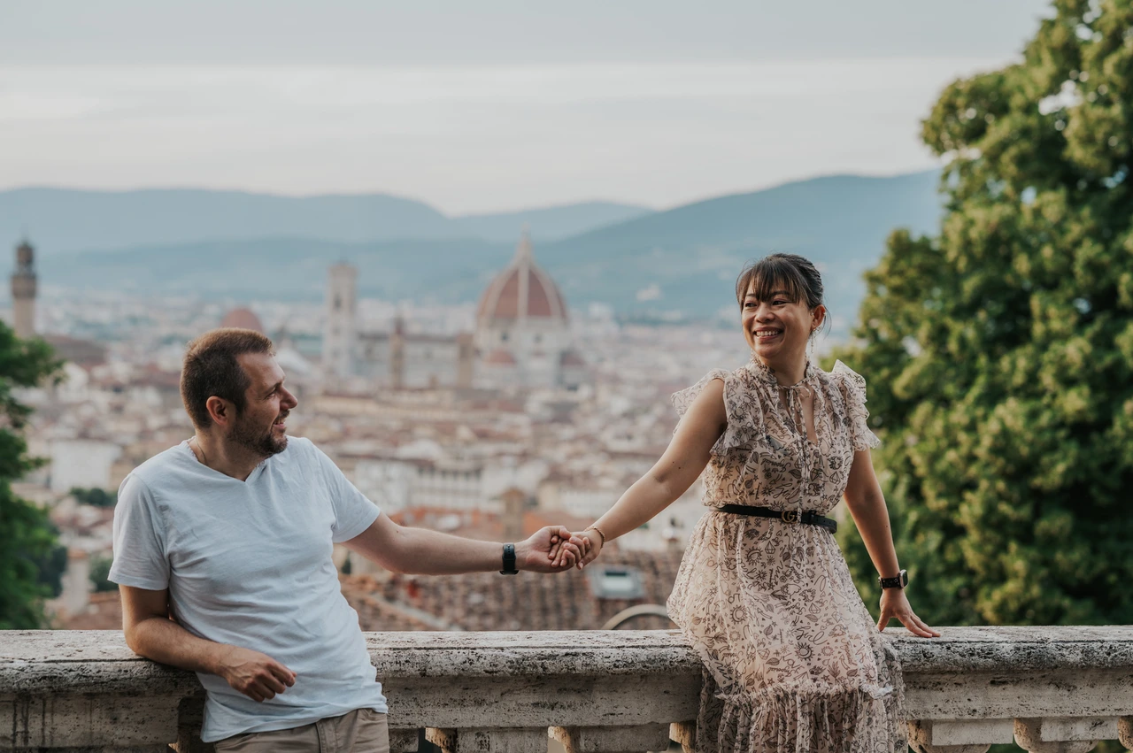 Florence photoshoot holding hands at the balustrade edge The couple hold hands beside the stone balustrade during their Florence photoshoot, with the city and leafy trees behind them.