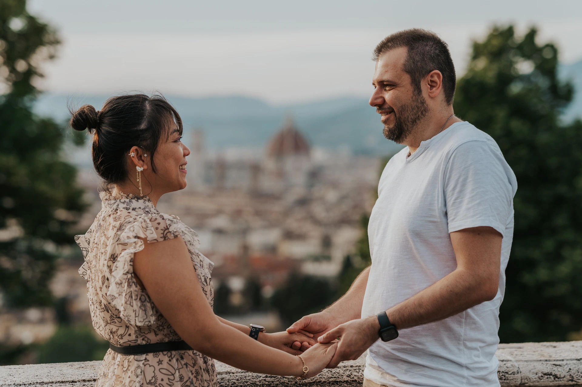 The couple hold hands beside the stone balustrade, with Florence and its hills behind them during their couple photoshoot.