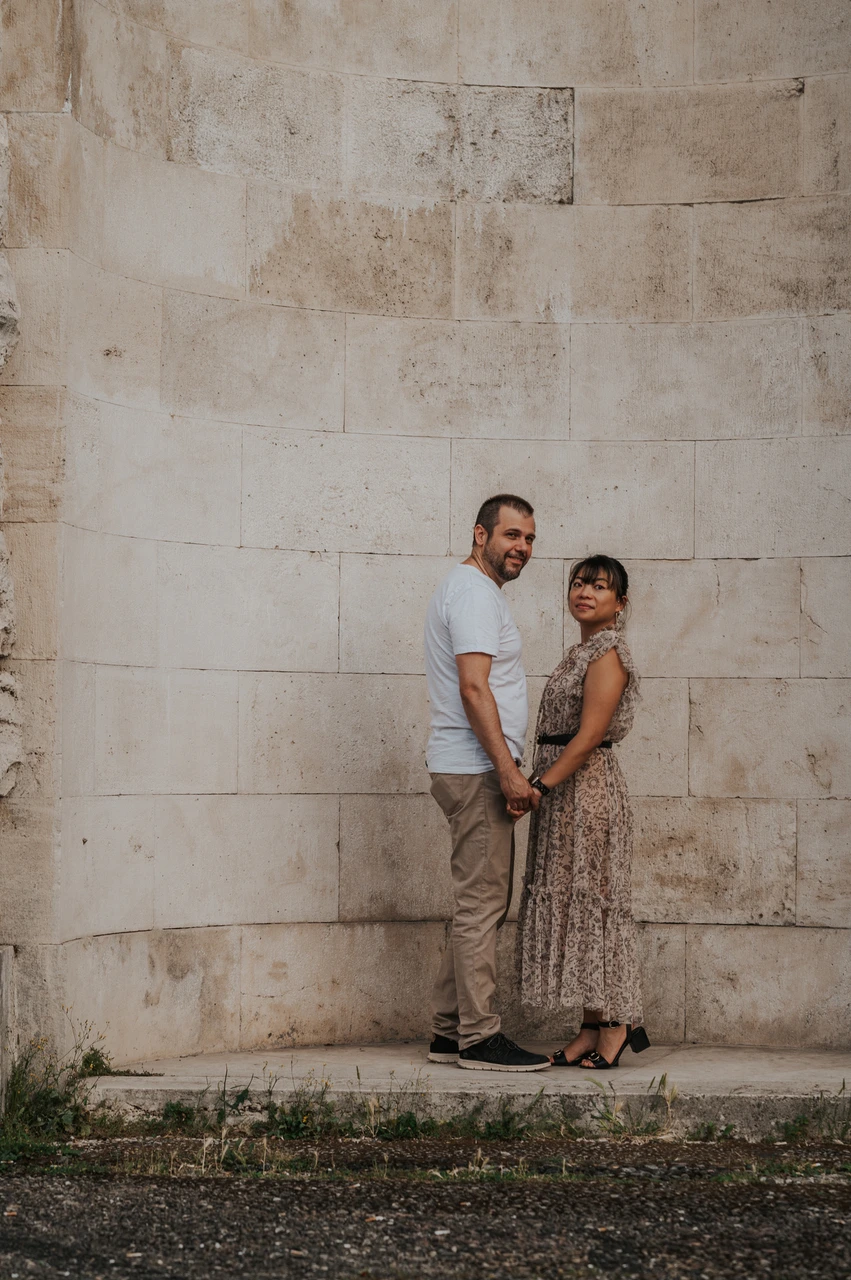 Florence photoshoot portrait against the pale stone recess The couple stand close together and smile towards the camera against the pale stone wall of an arched recess during their Florence photoshoot.