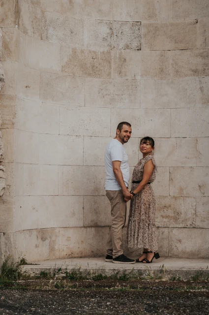 Florence photoshoot portrait against the pale stone recess The couple stand close together and smile towards the camera against the pale stone wall of an arched recess during their Florence photoshoot.