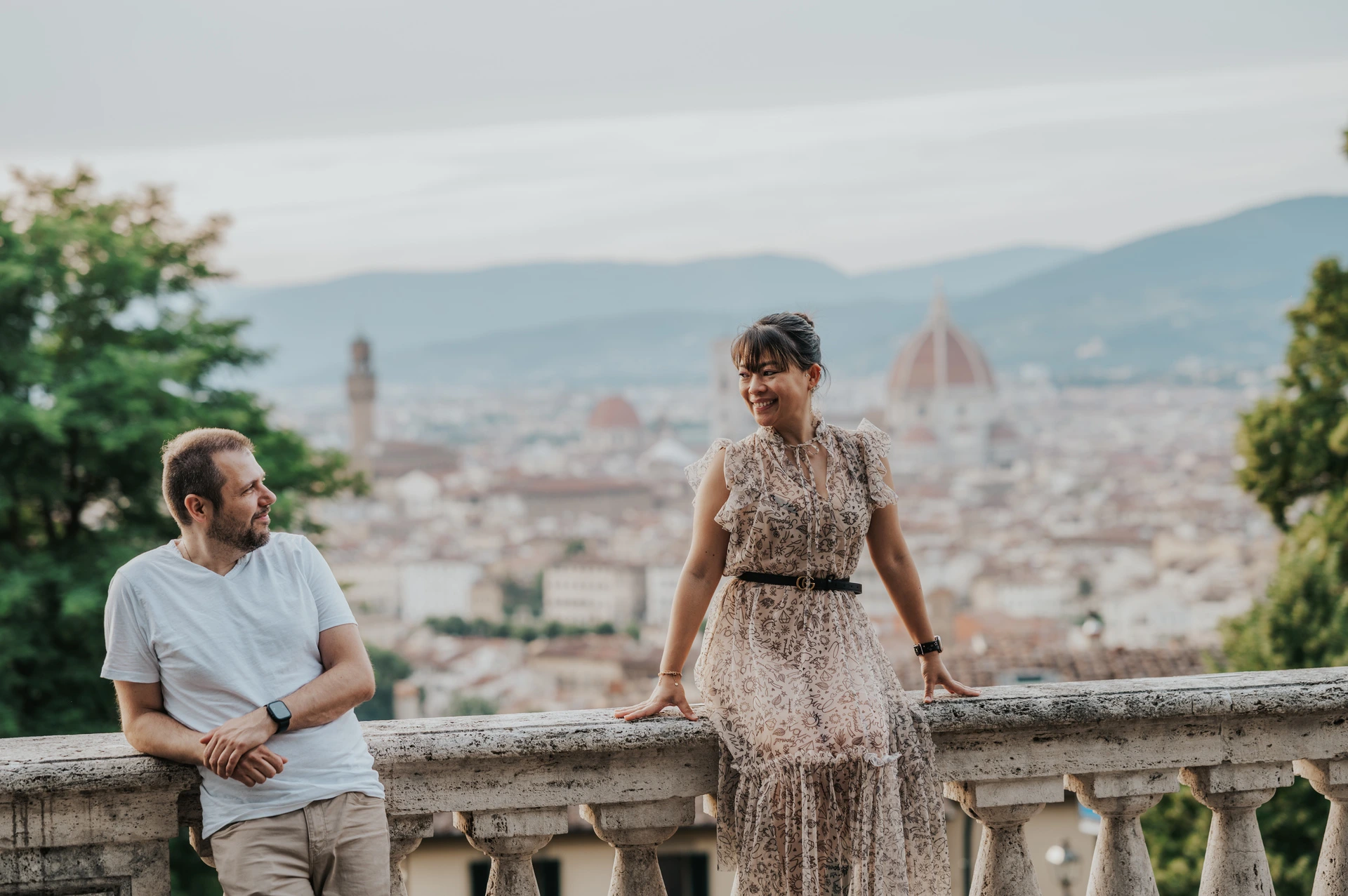 The man leans against the balustrade beside the woman during their Florence photoshoot, with the Duomo behind them.