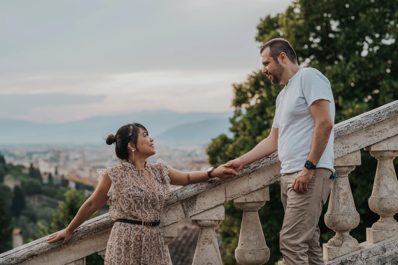 Florence photoshoot beside the stone stair rail The couple hold hands beside the sloping stone stair rail during their Florence photoshoot, with Florence rooftops visible between the trees.