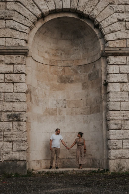 Florence photoshoot beneath a tall stone arch The couple hold hands at the base of a tall arched stone recess in their Florence photoshoot, with the full stonework filling the portrait.