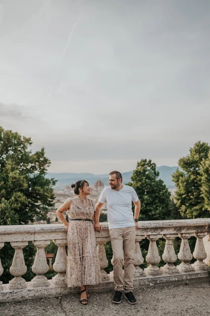 Full-length Florence photoshoot by the viewpoint balustrade The couple lean beside the stone balustrade in a full-length Florence photoshoot portrait, framed by trees and the city below.