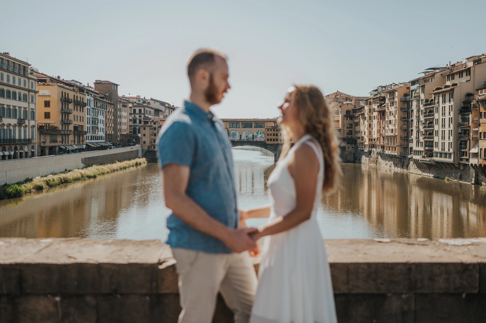 Ponte Vecchio is in focus behind the softly blurred couple facing each other during their Florence photoshoot.