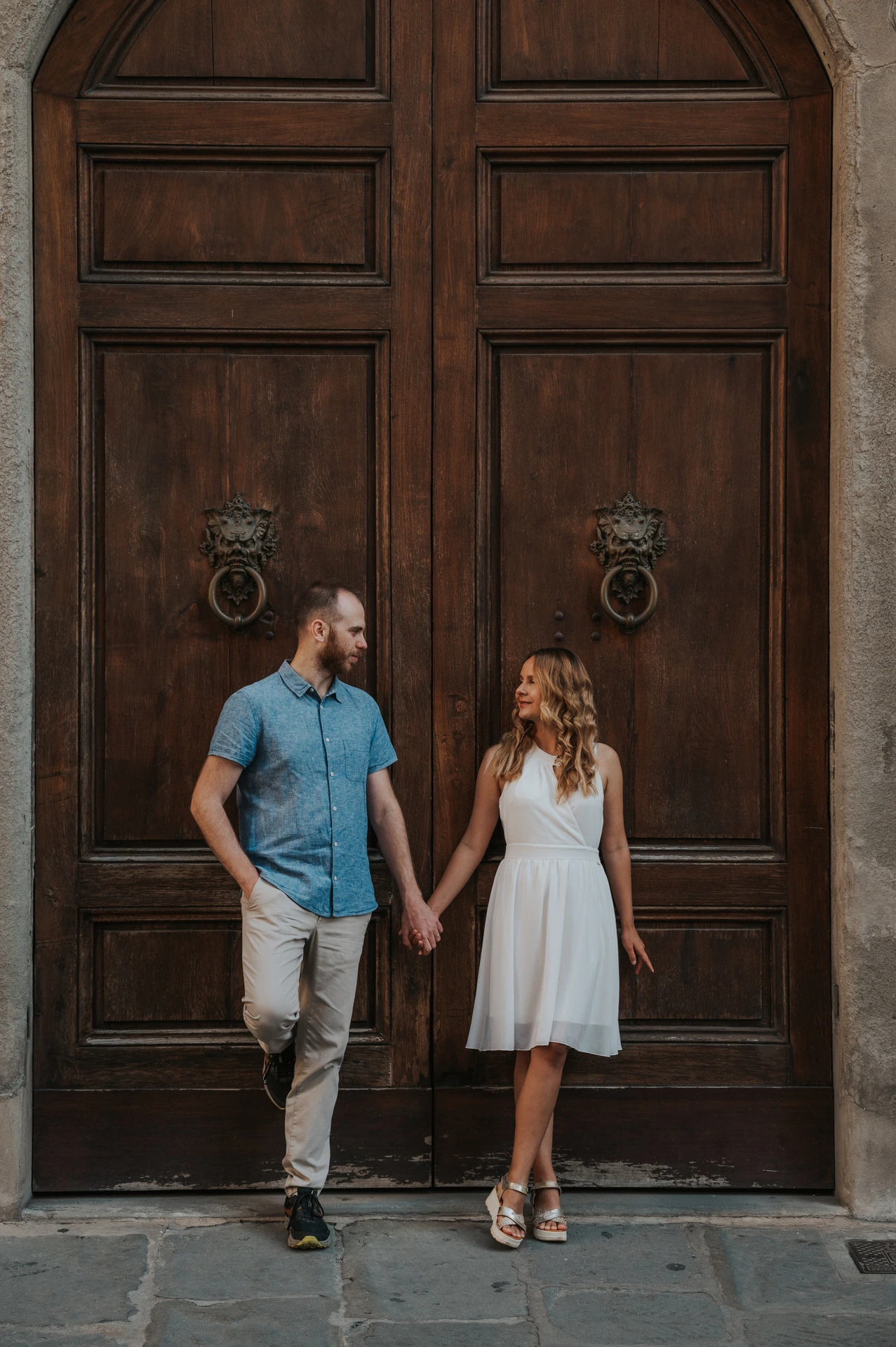 The couple walk hand in hand in front of a dark wooden door during their Florence couple photoshoot.