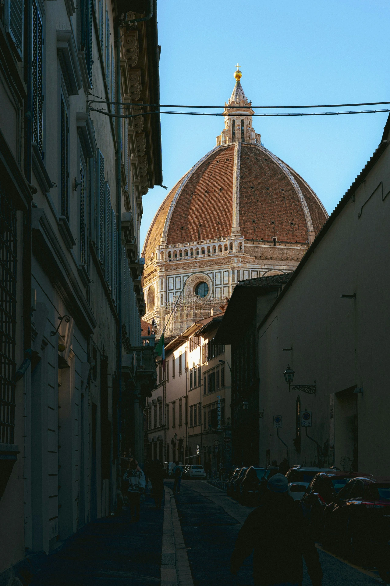 Florence Cathedral dome framed by a narrow city street with people walking below