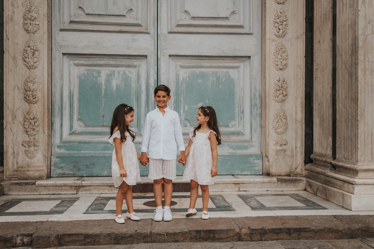 The children together at the doorway in a Florence family photoshoot The three children hold hands and look towards one another in front of the green door during their Florence photoshoot.