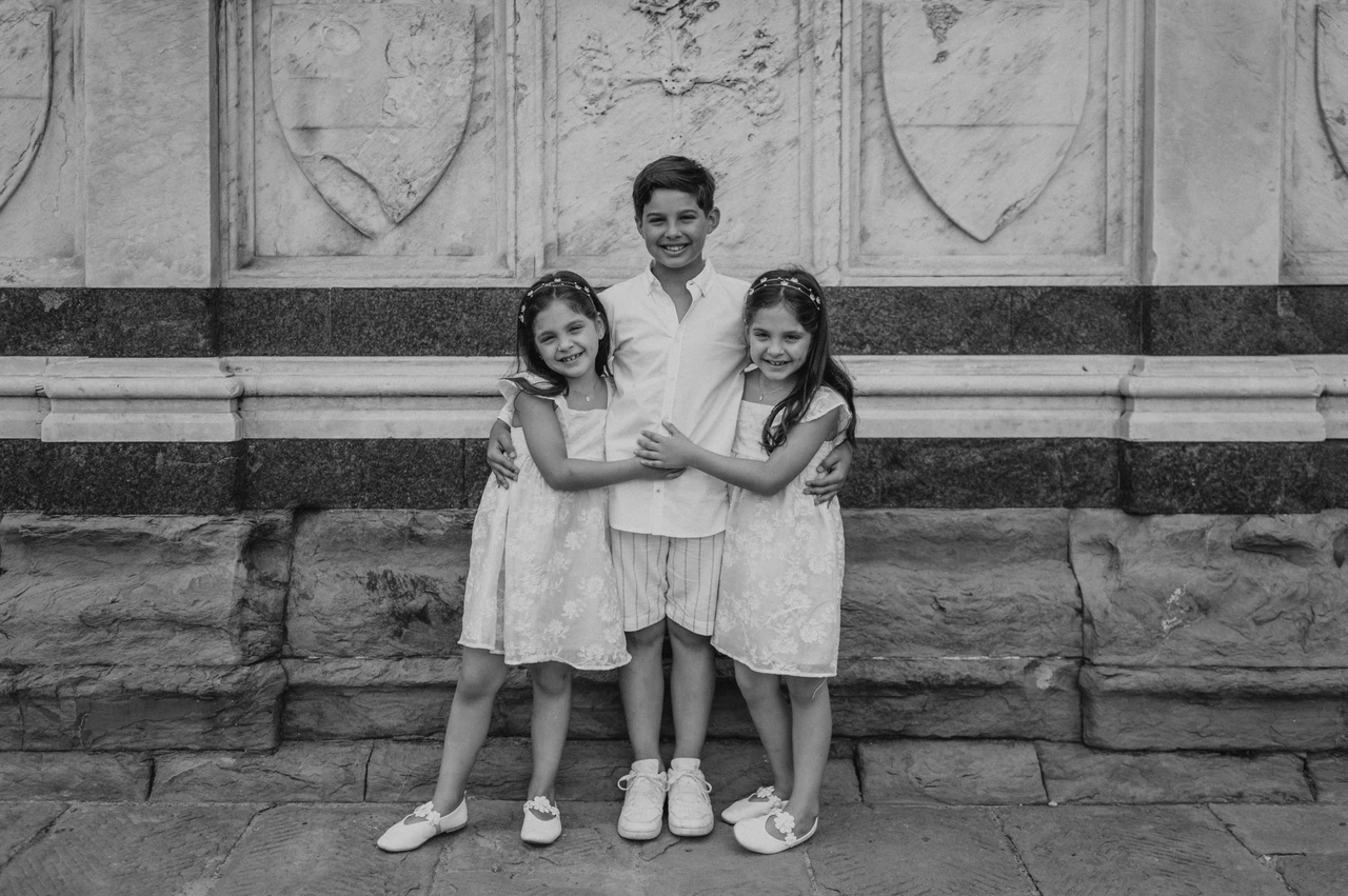 Florence family photoshoot with a black-and-white portrait of the children Black-and-white photograph of the three children hugging beside the carved marble wall during their Florence family photoshoot.