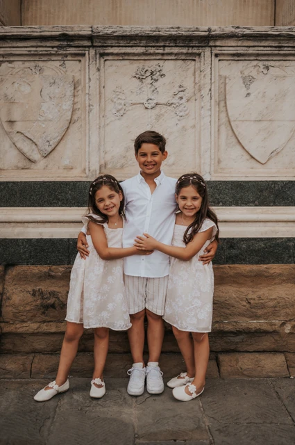 The three children hug in front of a carved marble wall and stone ledge during their Florence family photoshoot.