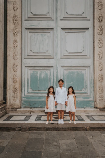 Florence family photoshoot with the children at the green doorway Three children stand holding hands below a tall green door during their Florence family photoshoot.