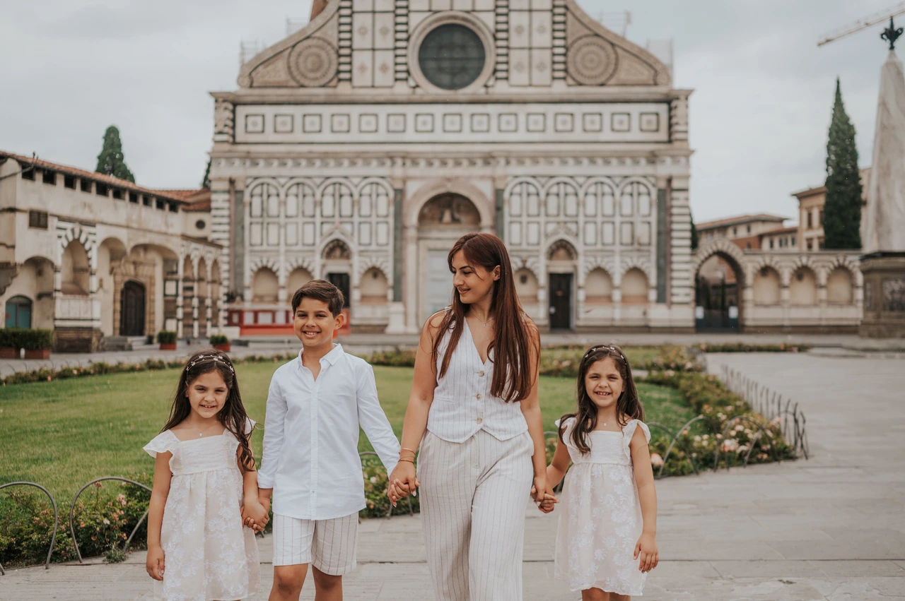 Florence family photoshoot with Santa Maria Novella in the background The family hold hands beside flowerbeds with Santa Maria Novella’s patterned facade behind them during their Florence photoshoot.