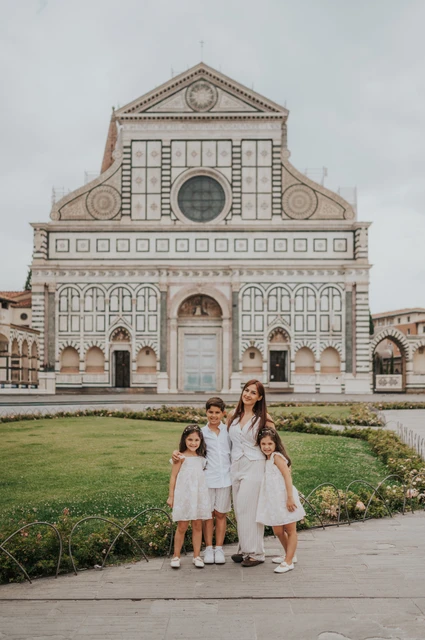 Florence family photoshoot on the square at Santa Maria Novella The family walk together on the square beside the flowerbeds, with Santa Maria Novella behind them, during their Florence family photoshoot.