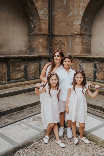 Florence family photoshoot with white outfits and warm stone The family pose together in white outfits beside a railing and warm stone walls during their Florence family photoshoot.