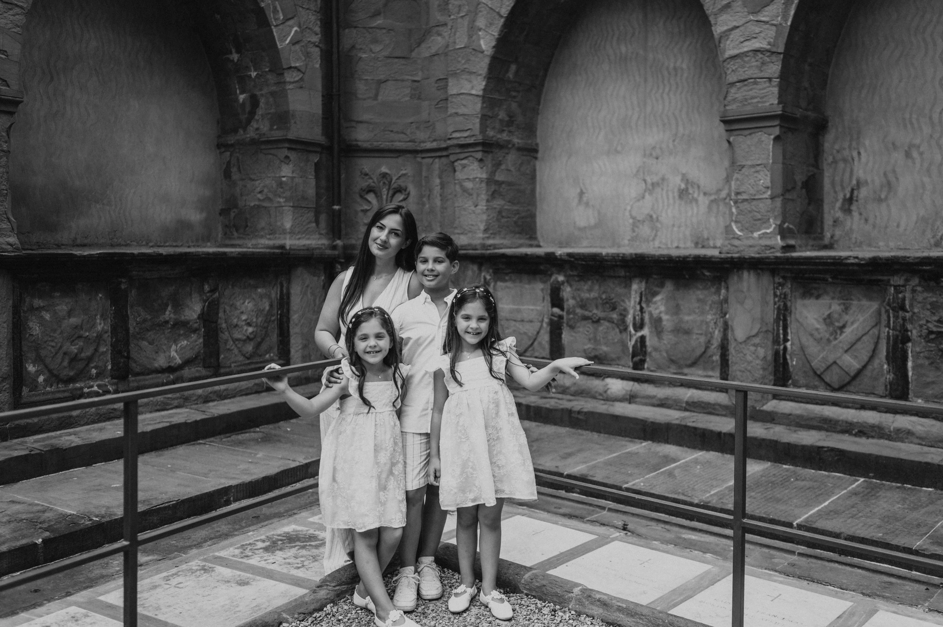 Black-and-white photograph of the family beside a railing and stone arches during their Florence family photoshoot.