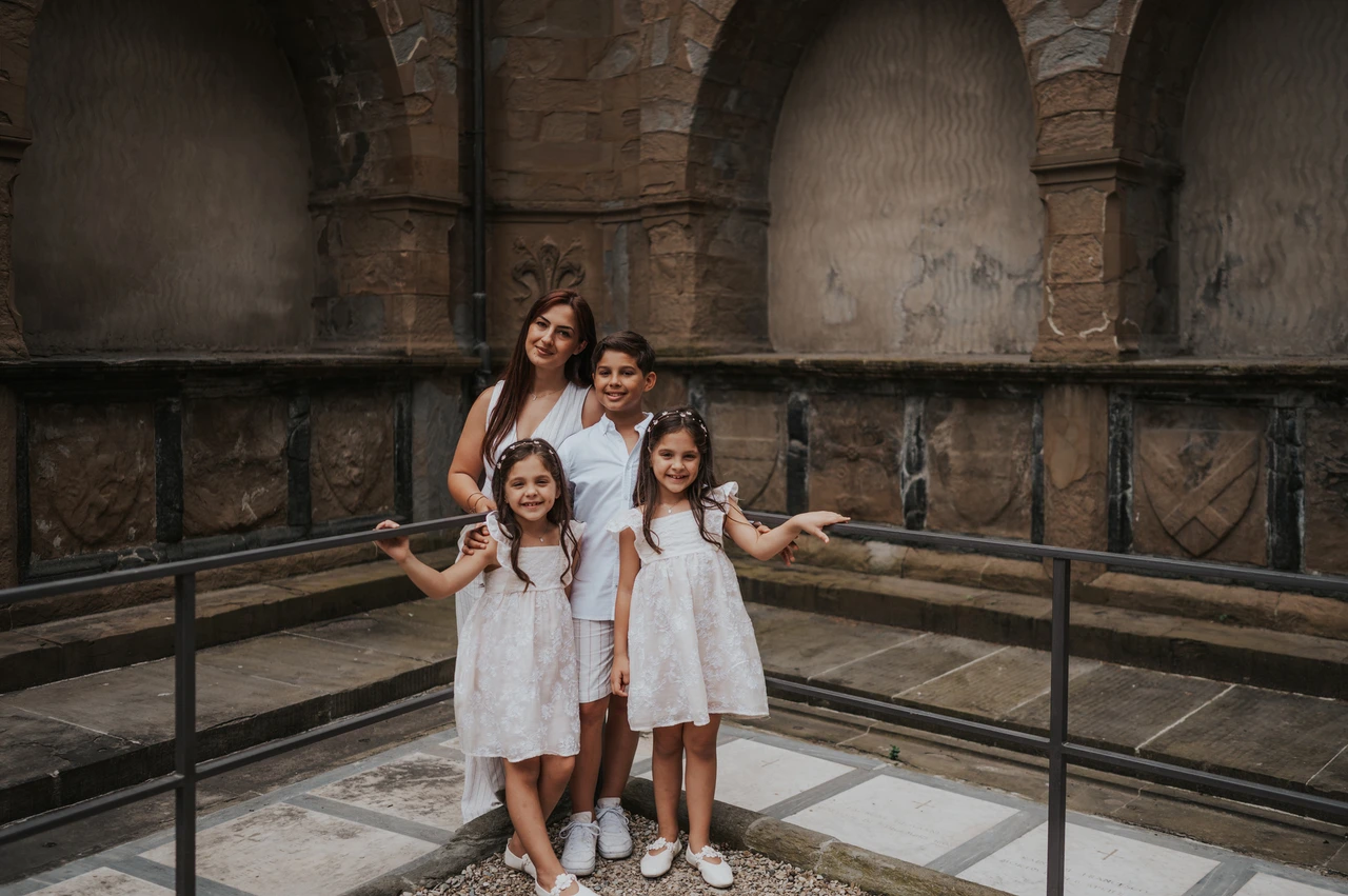 Florence family photoshoot beside weathered stone arches The family stand together by a metal railing and weathered stone arches during their Florence photoshoot.
