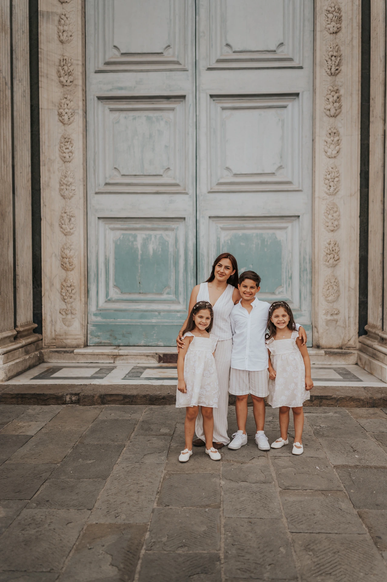 The family of four stand together beneath a tall green door framed by carved marble during their Florence family photoshoot.