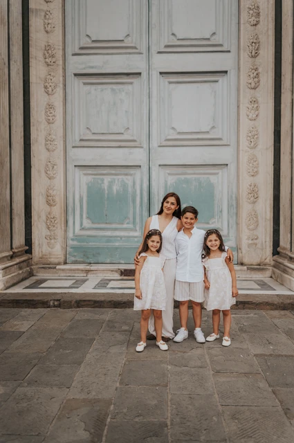 Florence family photoshoot beneath a tall marble doorway The family of four stand together beneath a tall green door framed by carved marble during their Florence family photoshoot.