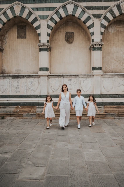 Florence family photoshoot framed by striped arches The family of four walk across the stone paving beneath striped arches during their Florence family photoshoot.