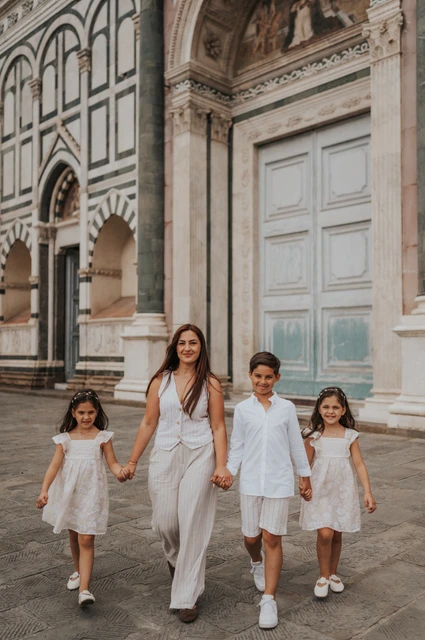 The family walk hand in hand past a green door and striped marble arches during their Florence family photoshoot.