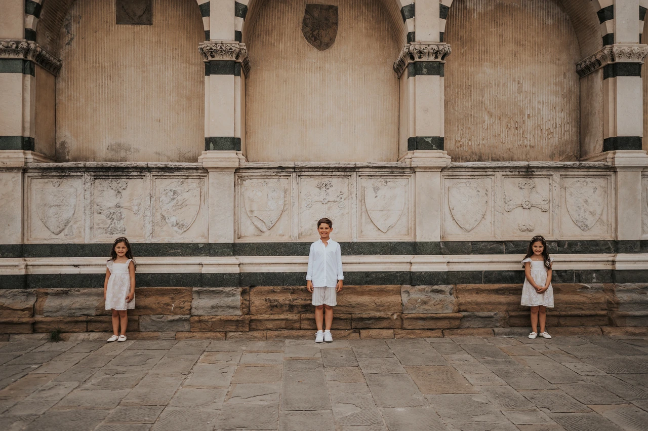 Florence family photoshoot beneath the striped marble arches The three children stand spaced apart below striped marble arches during their Florence family photoshoot.