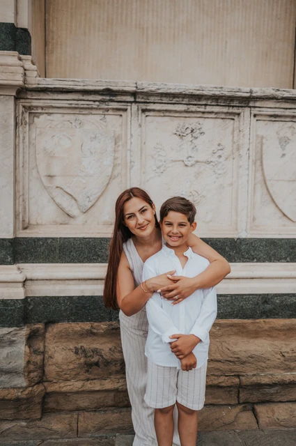 A close family portrait of a woman and boy during a Florence photoshoot A woman and boy smile together beside the marble wall during their Florence family photoshoot.