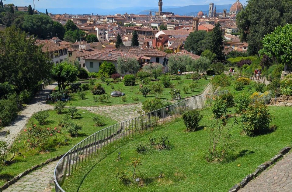 A green hillside garden opens toward Florence's terracotta rooftops, with the cathedral dome rising above the city.