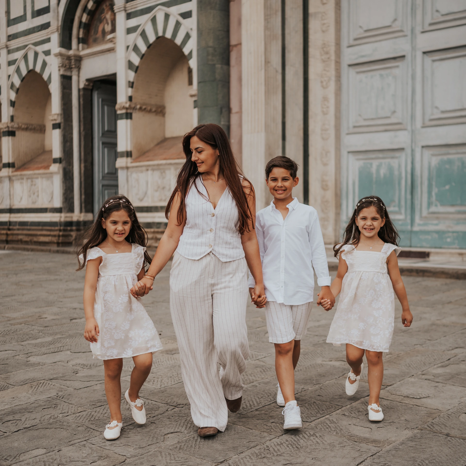 Una donna e tre bambini si tengono per mano davanti a una facciata in marmo decorato a Firenze.