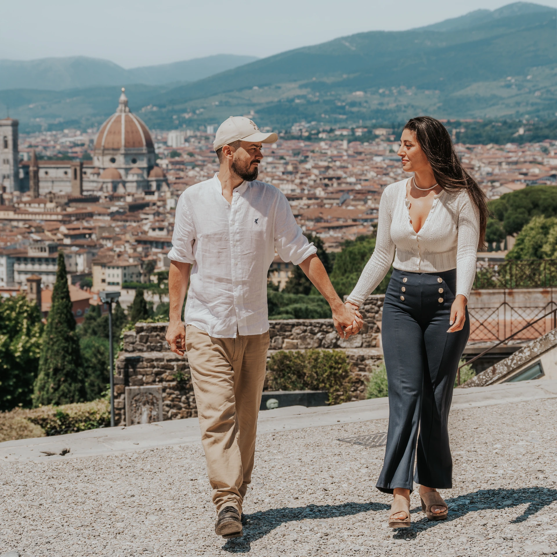 Una coppia cammina mano nella mano a San Miniato al Monte, con i tetti di Firenze e la cupola del Duomo alle spalle.