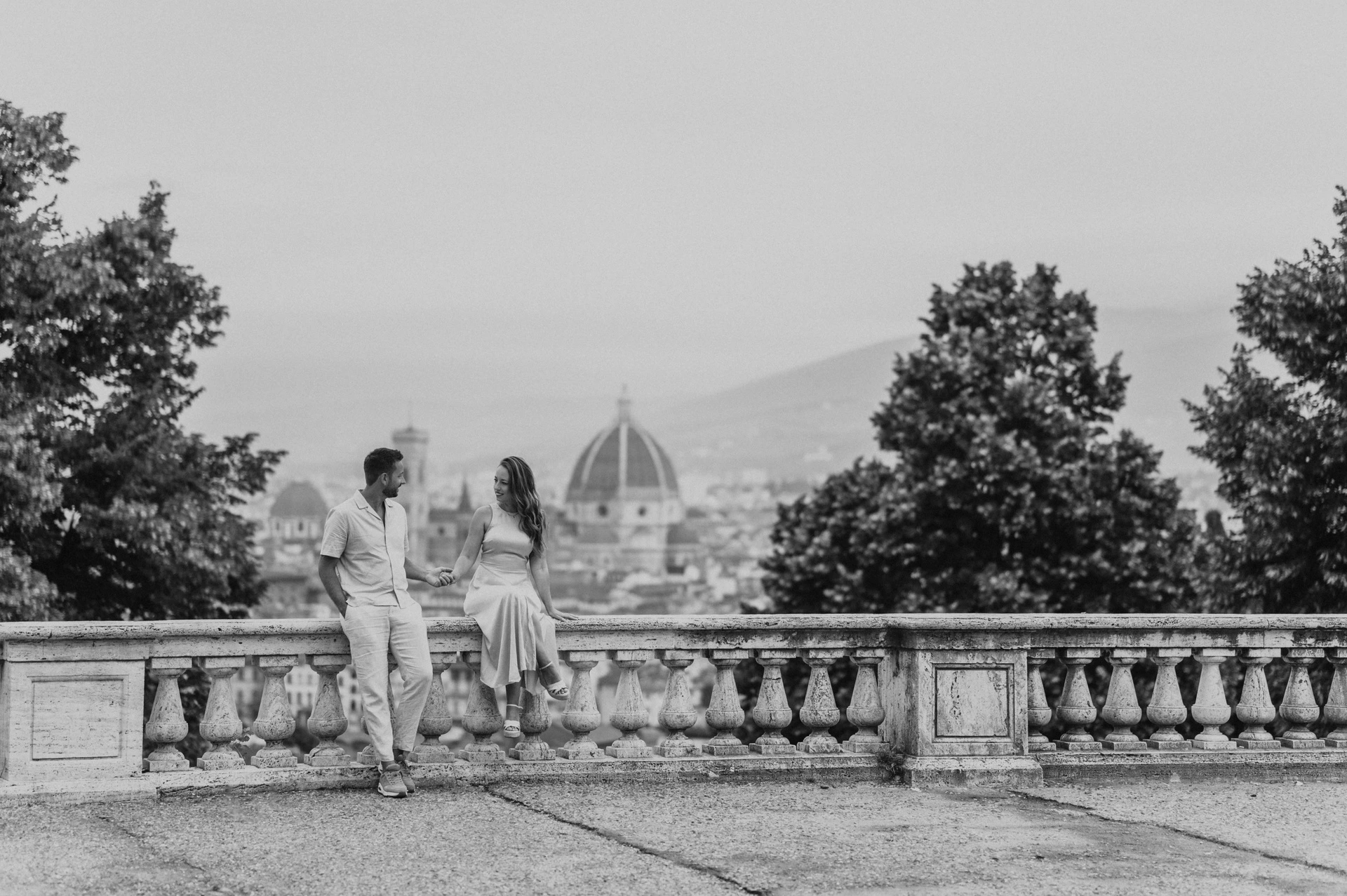 Black-and-white photograph of the couple together by the balustrade, with one partner seated, during their Florence proposal photoshoot.