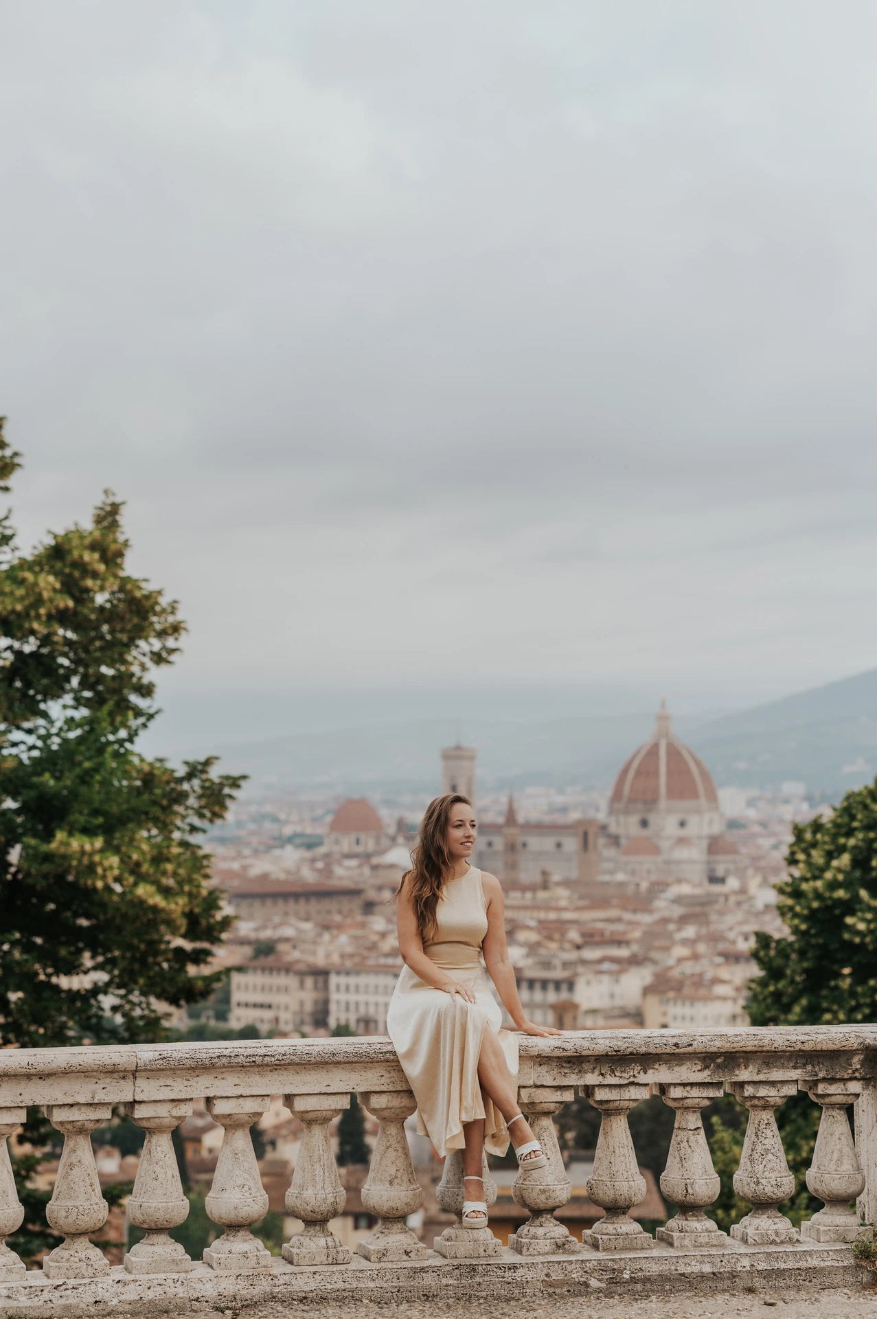 She sits in a cream dress on the stone balustrade above Florence during the proposal photoshoot.