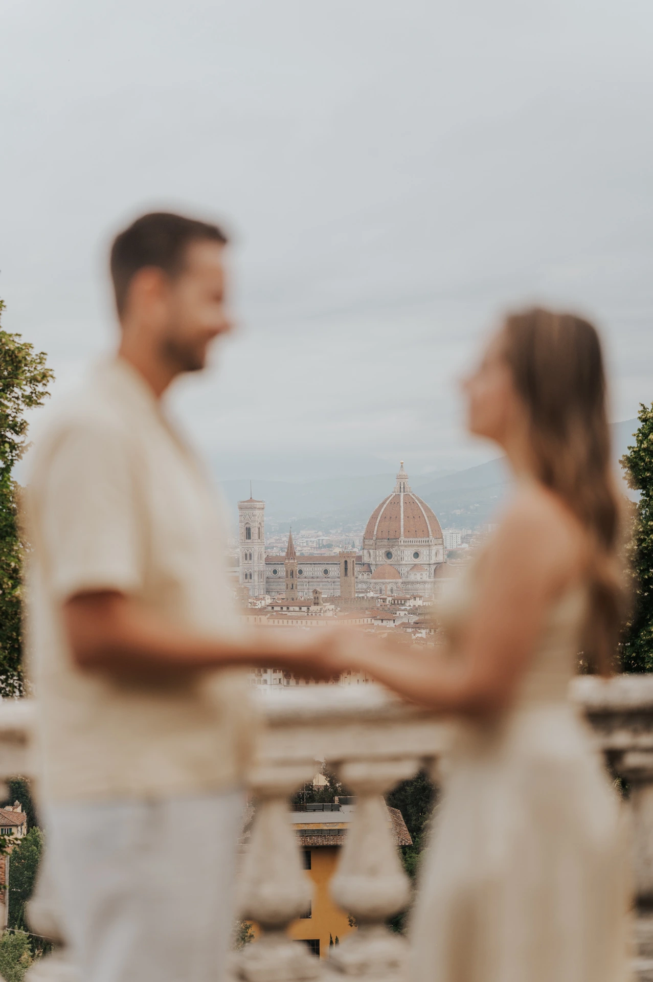 Florence’s Duomo is in focus behind the softly blurred couple holding hands during their proposal photoshoot at San Miniato al Monte.