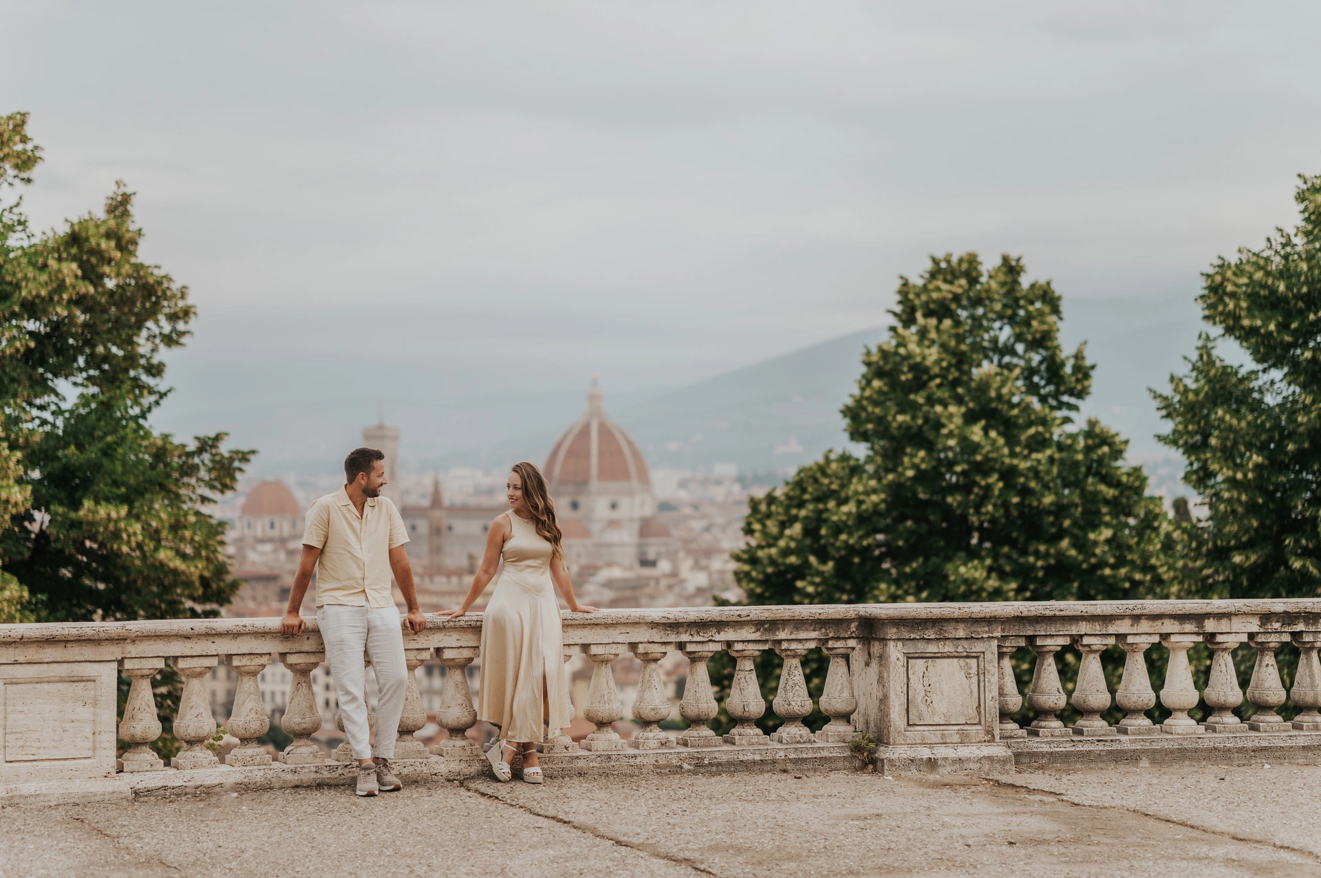Florence proposal photoshoot beside the viewpoint balustrade The couple stand holding hands beside the viewpoint balustrade with trees and Florence’s Duomo behind them during their proposal photoshoot.