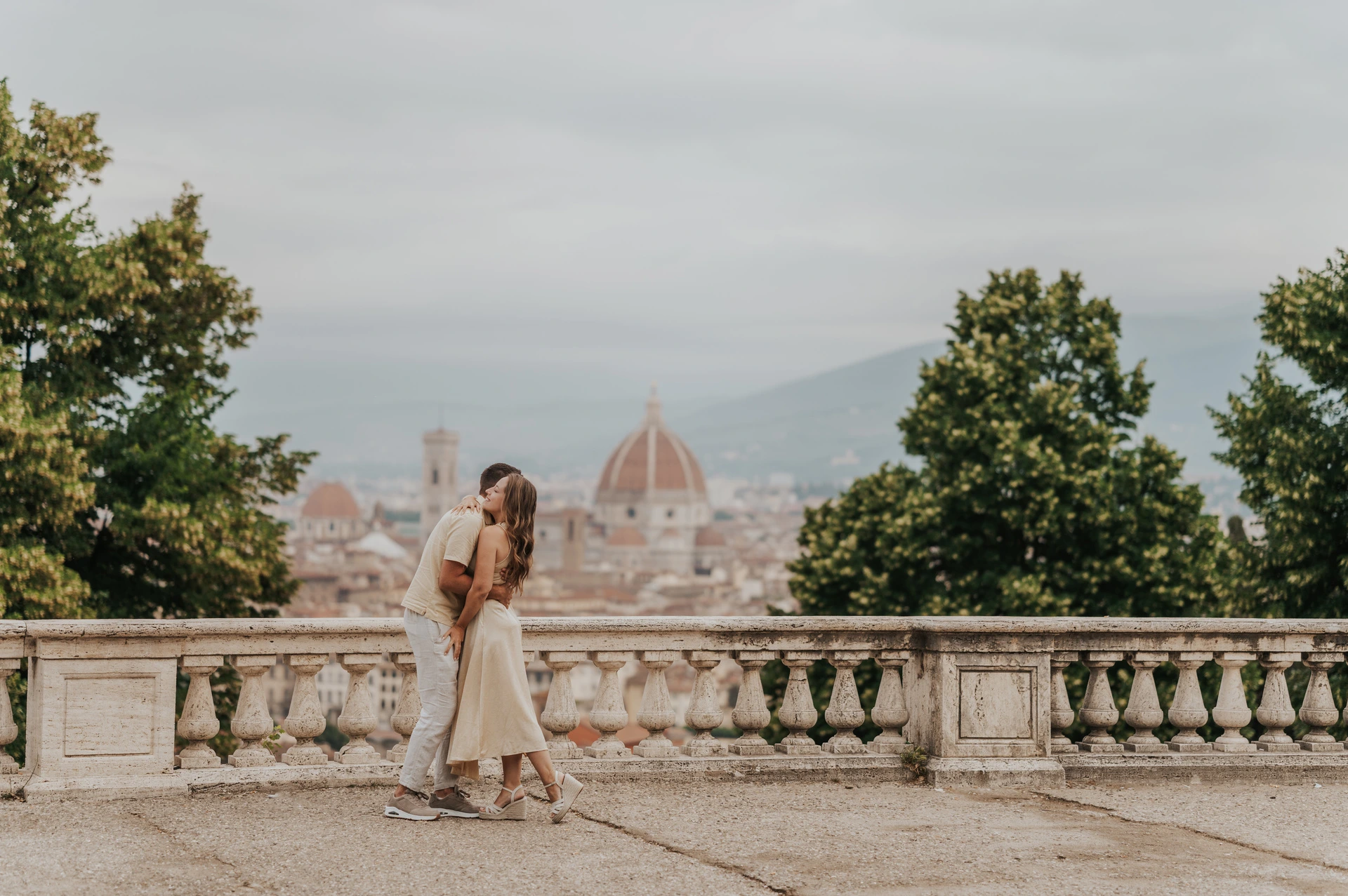 The couple share a kiss beside the stone balustrade with the Duomo beyond them during their Florence proposal photoshoot.