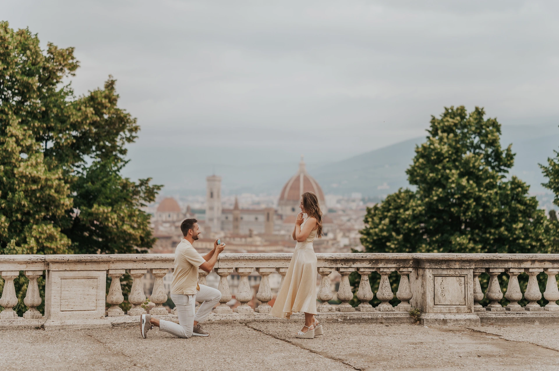 The proposal moment during a Florence photoshoot at San Miniato A wide view of the couple beside San Miniato al Monte’s stone balustrade during their Florence proposal photoshoot, with the Duomo behind them.
