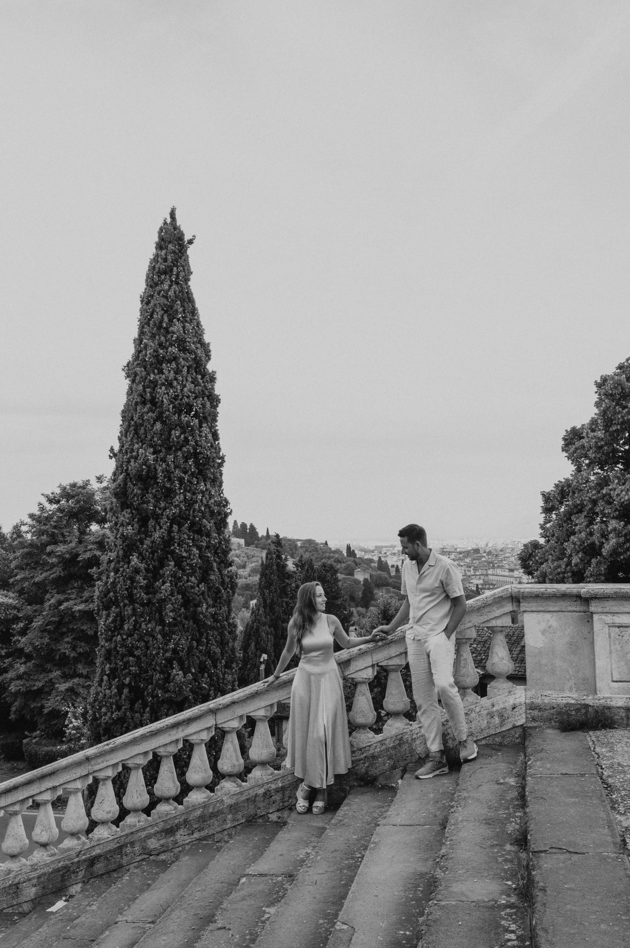 Black-and-white portrait of the couple on stone steps beneath a tall cypress during their Florence proposal photoshoot.