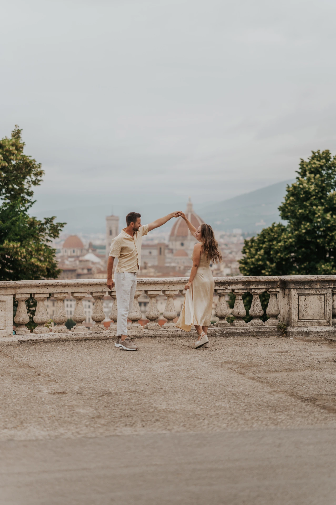 He raises her hand as she turns beside the stone balustrade during their Florence proposal photoshoot.