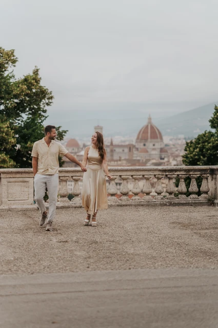 A walk together during a Florence proposal photoshoot The couple walk hand in hand across the viewpoint with Florence’s cathedral dome in the distance during their proposal photoshoot.