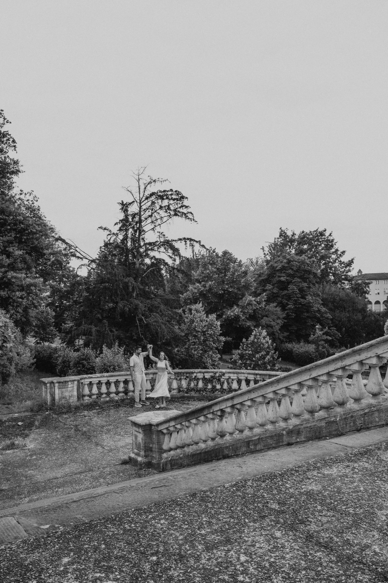 Black-and-white view of the couple among the stone stairs, balustrades and trees during their Florence proposal photoshoot.
